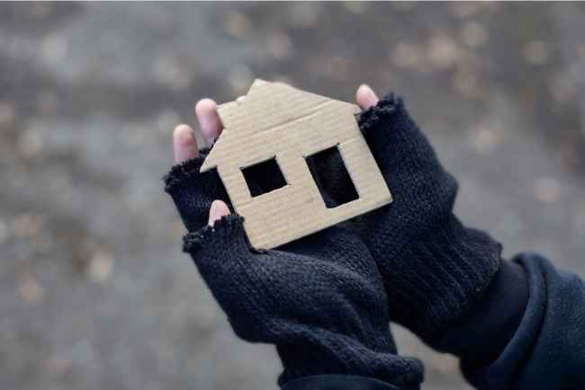 Hands with fingerless gloves holding a cardboard cutout of a house