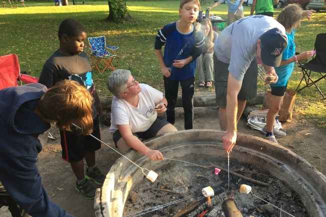 Adults and kids gathering around a firepit roasting marshmallows