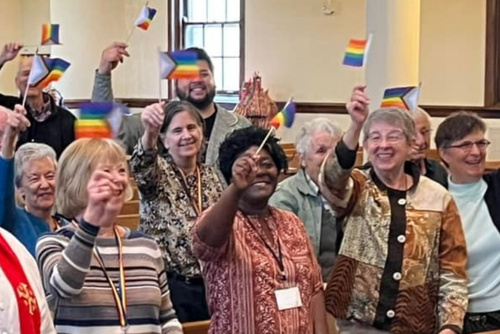 church members in the pews during worship standing waving pride flags